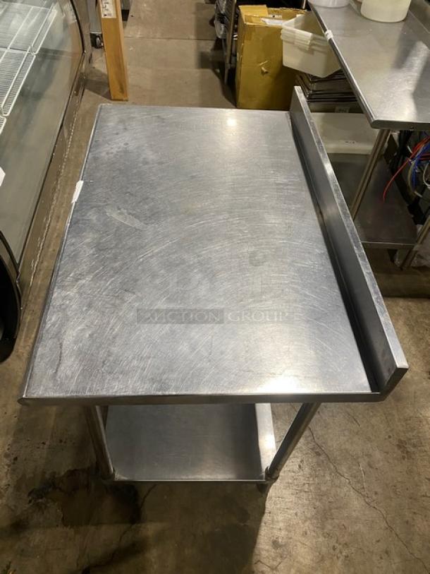 Commercial stainless steel worktop table with undershelf, up-turned backsplash, and sturdy legs. Surface shows light wear.