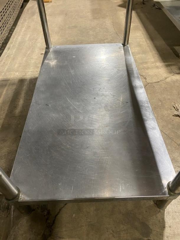 Commercial stainless steel worktop table with single undershelf, up-turned back splash, and legs. Scratched surface.