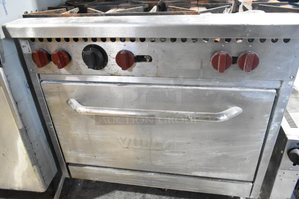 Vulcan stainless steel commercial gas 6-burner range with oven, over shelf, and backsplash. Features red control knobs.