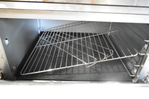 Vulcan stainless steel commercial oven interior, showing metal racks. Gas-powered, six burners, over shelf, and backsplash.