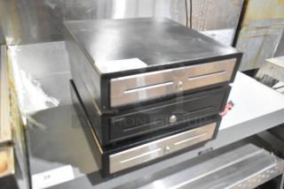 Three metal cash drawers with lockable fronts, stacked, black with silver accents. Slight wear visible.