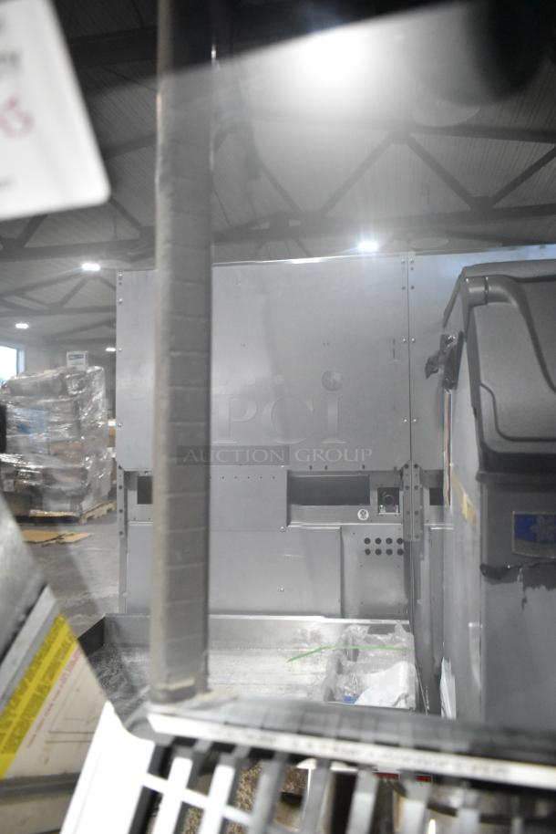 Industrial metal machinery with visible panels and fixtures, positioned indoors amidst warehouse environment.