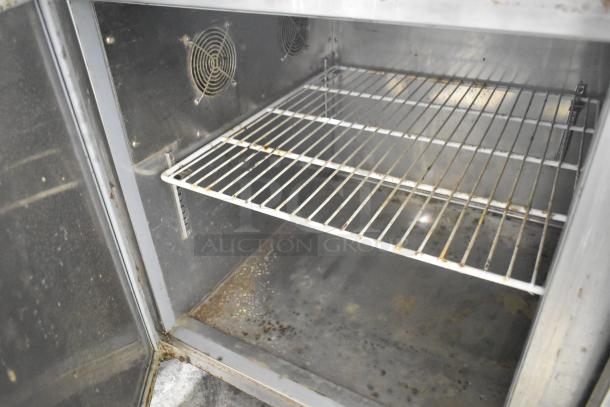 Avantco 178PICL2 stainless steel pizza prep table interior, showing wire shelf and fan; exhibits signs of use.