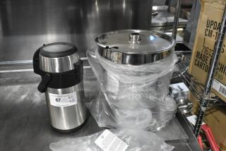 Brand new stainless steel air pot and cylindrical drop-in bin wrapped in plastic. Auction tag with quantity visible.