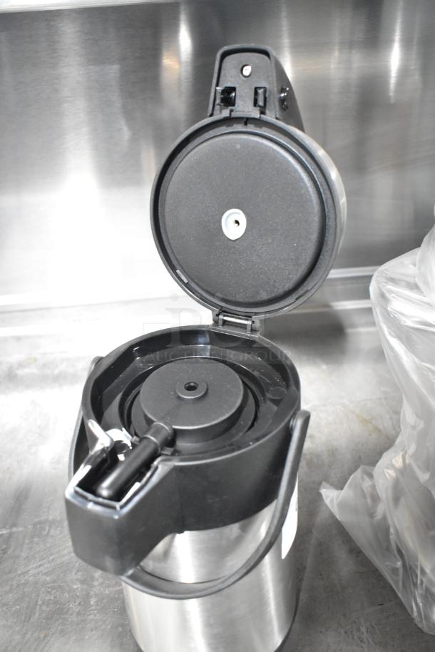 Stainless steel air pot with open lid, brand new, features a black handle and spout for easy pouring.