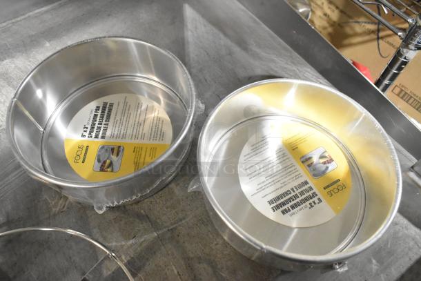 Two new 8" Focus non-stick springform baking pans with printed labels. Minor scratches visible. Auction includes a pie cutter.