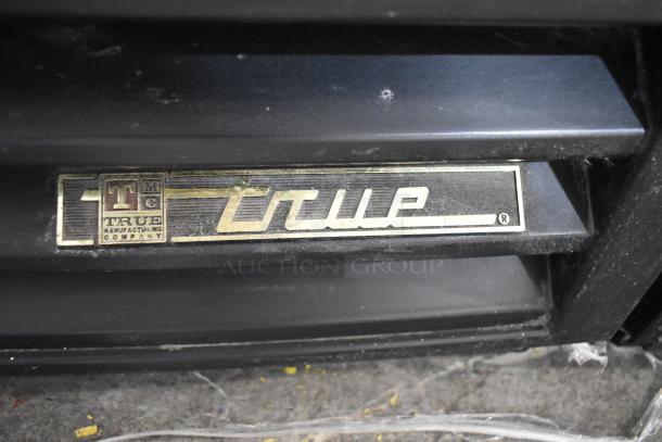 True GDM-12 cooler label with brand logo, part of a single door reach-in merchandiser, black metal finish.