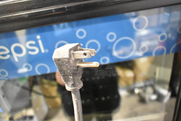 True GDM-12 cooler merchandiser plug detail, showing standard 115V electrical connection, set against a Pepsi-themed backdrop.