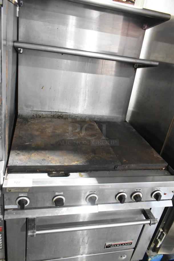Garland stainless steel commercial gas griddle with oven, overshelf, and backsplash. Used condition, visible wear.