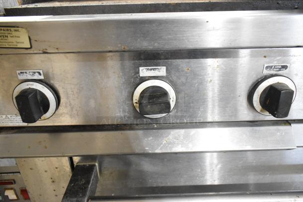 Garland stainless steel commercial gas griddle with three control knobs. Features show wear. Includes oven, overshelf, backsplash.