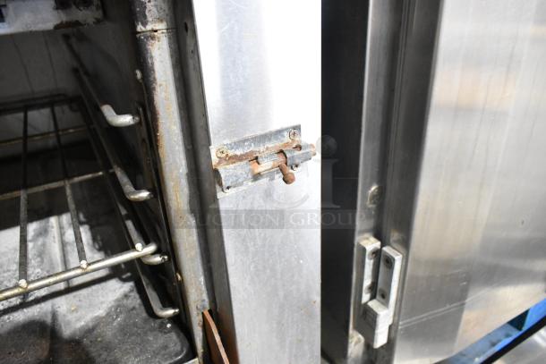 Garland stainless steel commercial gas flat top griddle with oven, shelf, and backsplash. Visible wear and rust on latch.