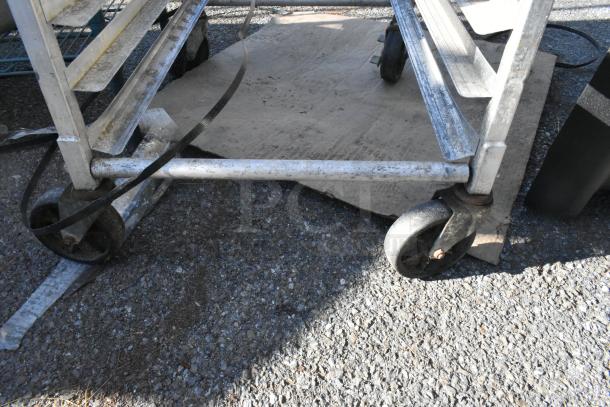 Metal commercial pan transport rack with sturdy commercial casters, shows signs of wear, ideal for kitchen use.