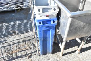 Blue Rubbermaid Slim Jim trash can with label, alongside a gray container and metal shelving, showing moderate wear.