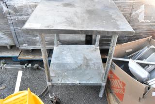 Stainless steel table with metal undershelf, on commercial casters, one caster missing. Used condition. Auction tag visible.