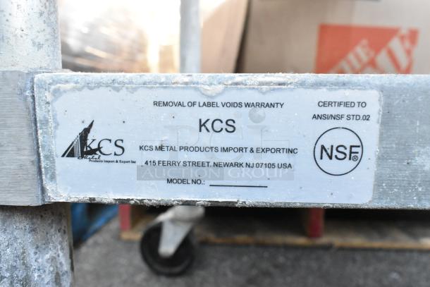 Stainless steel table with metal under shelf, on commercial casters; missing one caster. Label shows KCS, NSF certified.