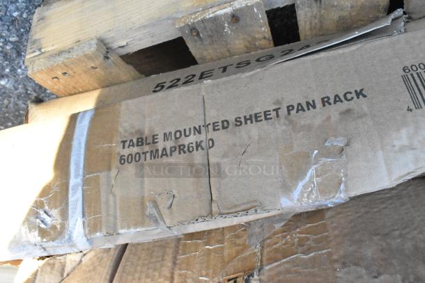 Cardboard box labeled "Table Mounted Sheet Pan Rack 600TMAPR6KD," showing signs of wear, on a wooden pallet.