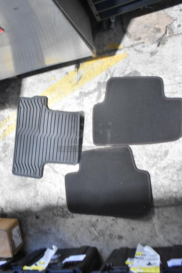 Black car mats, brand new, in a black poly bin. Various styles shown, including rubber and carpet textures.