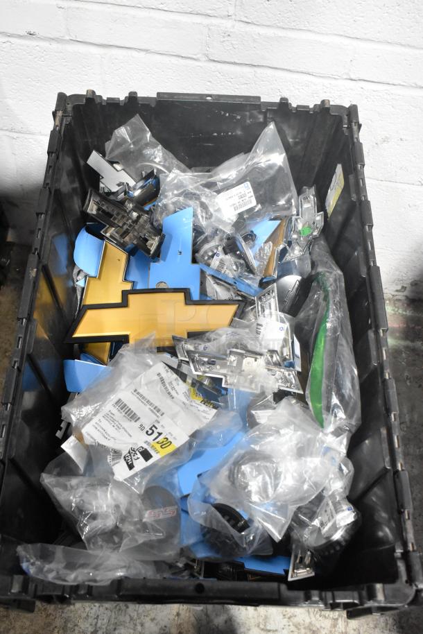 Brand new lot of various car parts in a black poly bin, featuring Chevy emblems in sealed plastic bags, with labels and markings visible.