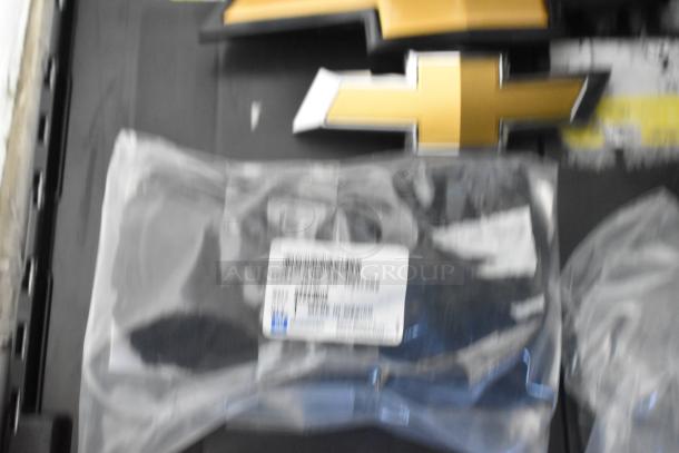 Brand new car parts in black poly bin, featuring Chevy emblems. Includes parts in sealed packages with visible labels.