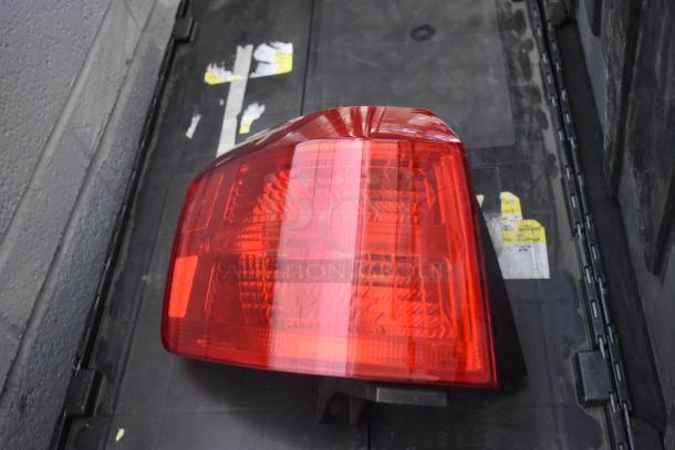 Brand new brake light in red, part of a lot of car parts, placed on a black poly bin. Tags visible, indicating new condition.