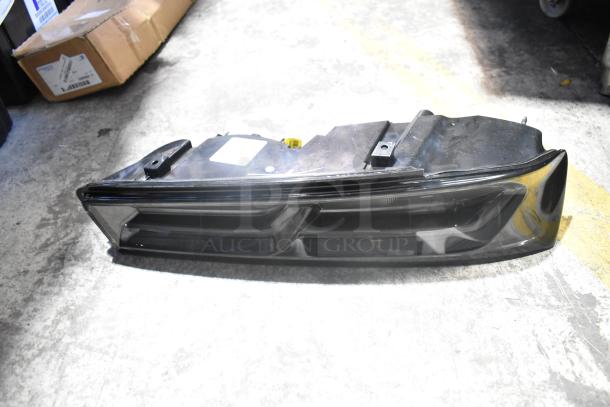 Brand new car brake light in black poly bin, pristine condition, includes Cadillac valve stem caps, visible label on top.