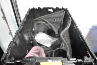 Black poly bin containing brand new car parts, including car mats and filter.
