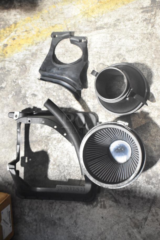 Brand new car parts, including Roush-branded intake components, displayed on a concrete floor.