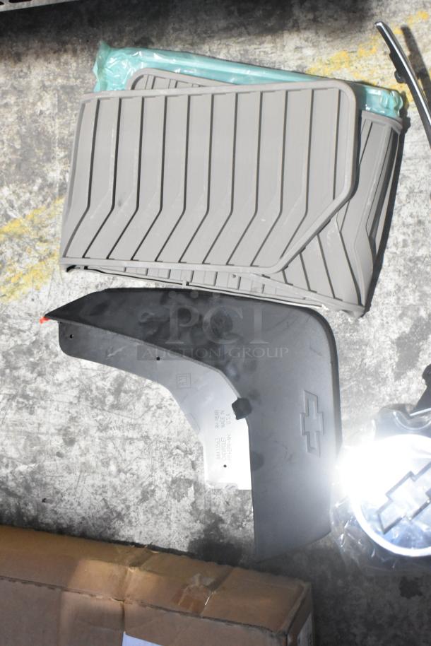 Brand new car parts lot including black car mats, mud flap with Chevrolet logo, and other components in a poly bin.