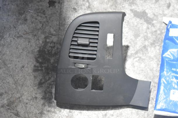 Black car interior panel with vent slots and switch, part of a brand new assorted car parts lot in poly bin.