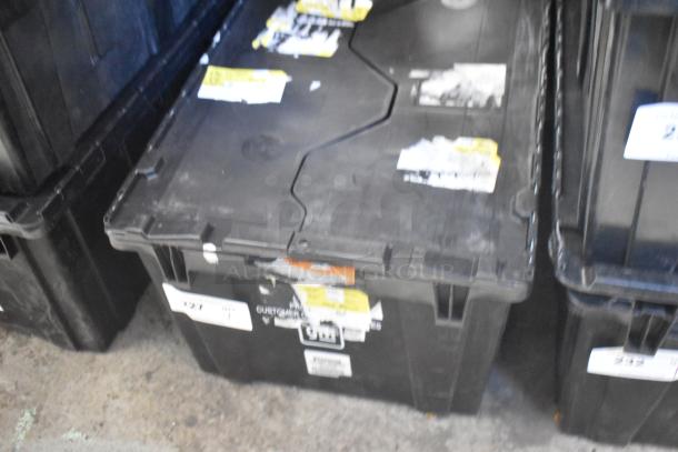 Black poly bin containing brand new GM car parts including grille assembly GM 10424821, lug nuts GM 19201541, and vertical cargo net GM 19244300. Bin has multiple labels and tags.