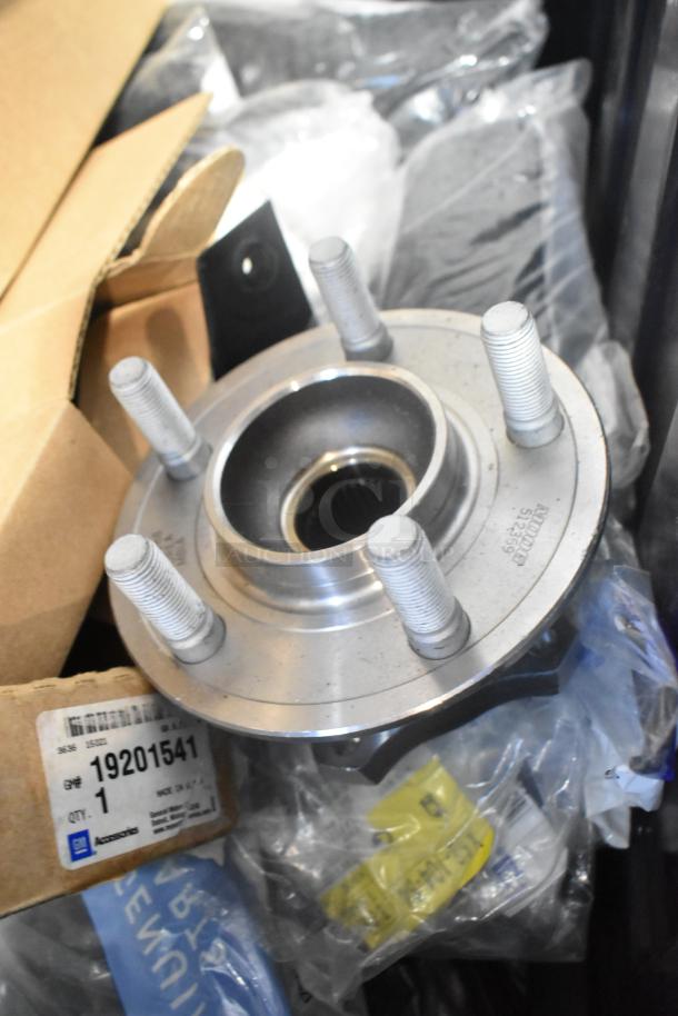 Brand new GM car parts in black poly bin, including 10424821 grille assy, 19201541 lug nuts, 19244300 cargo net.