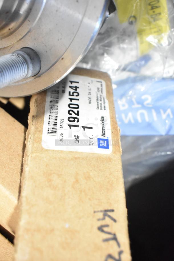 Brand new GM car parts including 10424821 grille assembly, 19201541 lug nuts, 19244300 cargo net in poly bin, labeled.