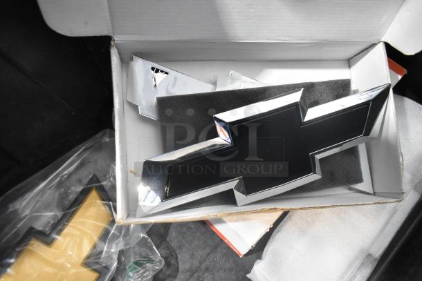 Brand new Chevrolet emblem in a foam-lined box, part of a lot including Corvette steering wheels in a black poly bin.