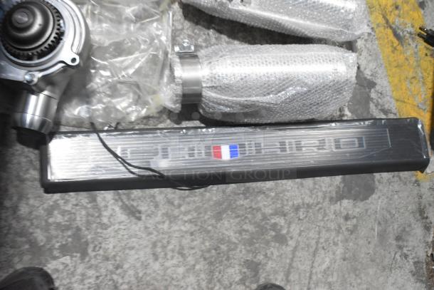 Lot of new car parts includes Corvette steering wheels, packaged in a black poly bin. Various parts visible with protective wrapping.