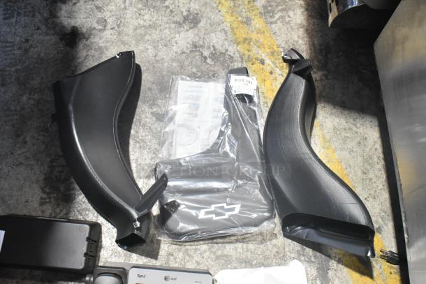 Lot of new car parts including black panels and AT&T SynJ telephone, in black poly bin. Features Chevy logo.