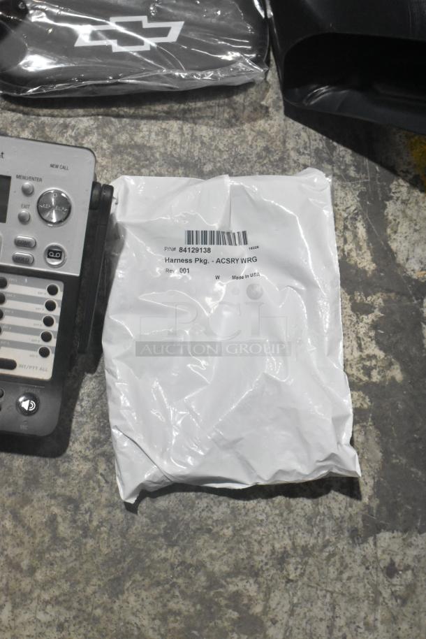 Brand new lot of car parts in a black poly bin, including a packaged wiring harness (P/N 84129138) and a telephone unit.