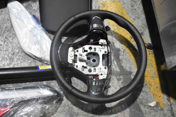 Lot of brand new car parts including a steering wheel and light panels, in a black poly bin. Steering wheel has control buttons.
