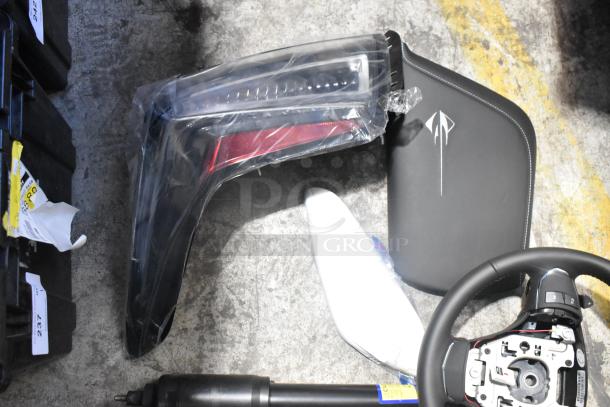 Brand new car parts lot in black poly bin, includes a steering wheel, light panels, and additional components.