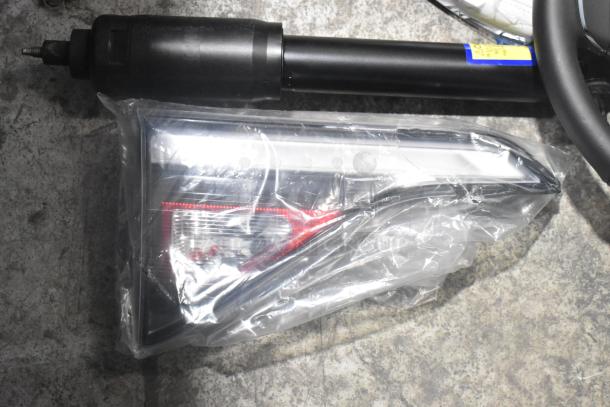 Brand new car parts lot, including light panels and steering wheel in black poly bin. Parts sealed in protective wrap.