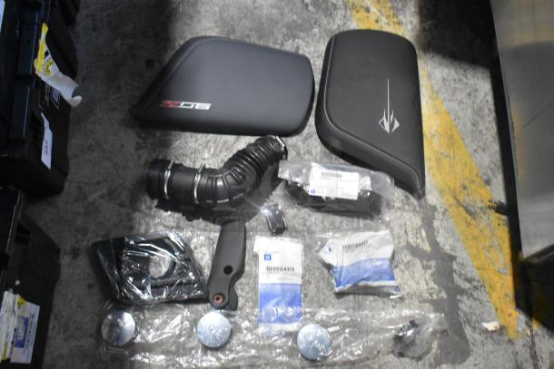 Brand new assorted car parts, including spark plugs, in a black poly bin. Parts include hoses, trim, and packaged items.