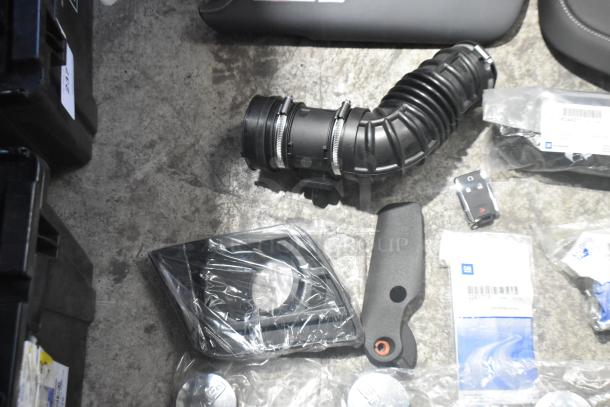 Lot of various brand new car parts including spark plugs, hoses, and covers, displayed in a black poly bin with visible GM labels.