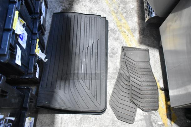 Brand new black car mats, textured design, alongside black storage bins with labels, on a concrete floor.