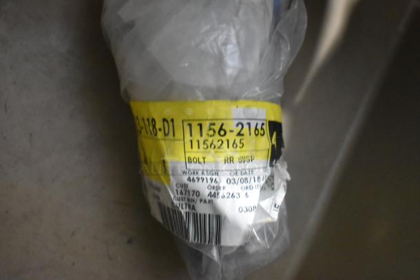 Lot of various new car parts in a tan poly bin, including car mats. Visible label reads: "BOLT RR SUSP."