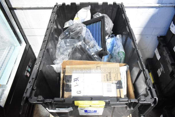 Black poly bin with various brand new car parts, including GMC emblems and GM wheel locks, in packaging.