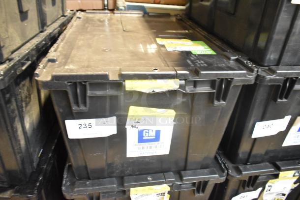 Black poly bin containing brand new various car parts, including GMC emblems and GM wheel locks, labeled with GM tags.