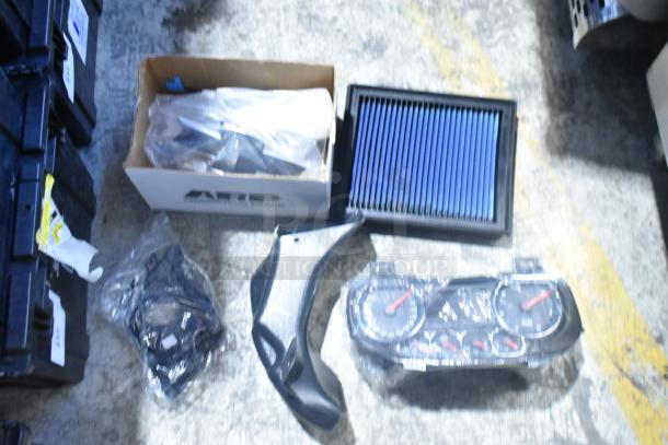 Brand new lot of car parts including GMC emblems, GM wheel locks in a black poly bin, featuring a new air filter.
