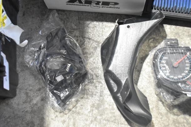 Lot of new car parts in black poly bin, includes GMC emblems and GM wheel locks, assorted in packaging.