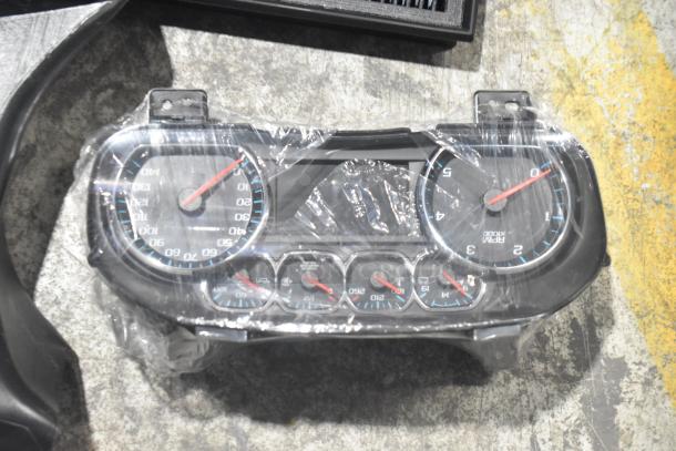 Brand new lot of various car parts including a speedometer cluster wrapped in plastic, part of a collection in a black poly bin.