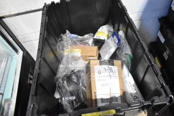 Brand new car parts in black poly bin, including GMC emblems and GM wheel locks, visible packaging and labels.