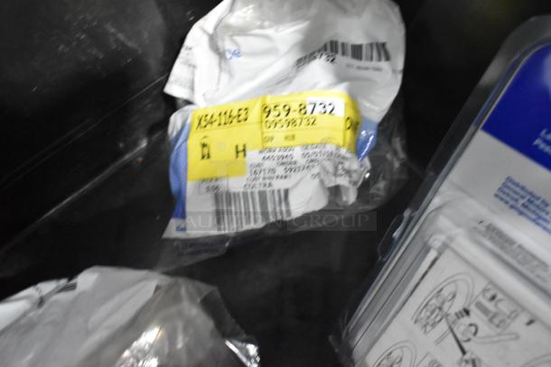 Brand new lot of various car parts, including GMC emblems and GM wheel locks, in black poly bin with visible label detailing part numbers.
